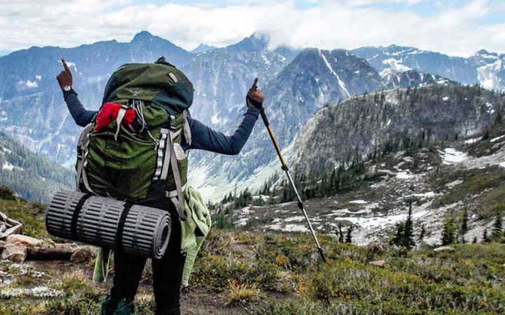 teen with raised hands looks out over mountain vista on backpacking expedition with outward bound